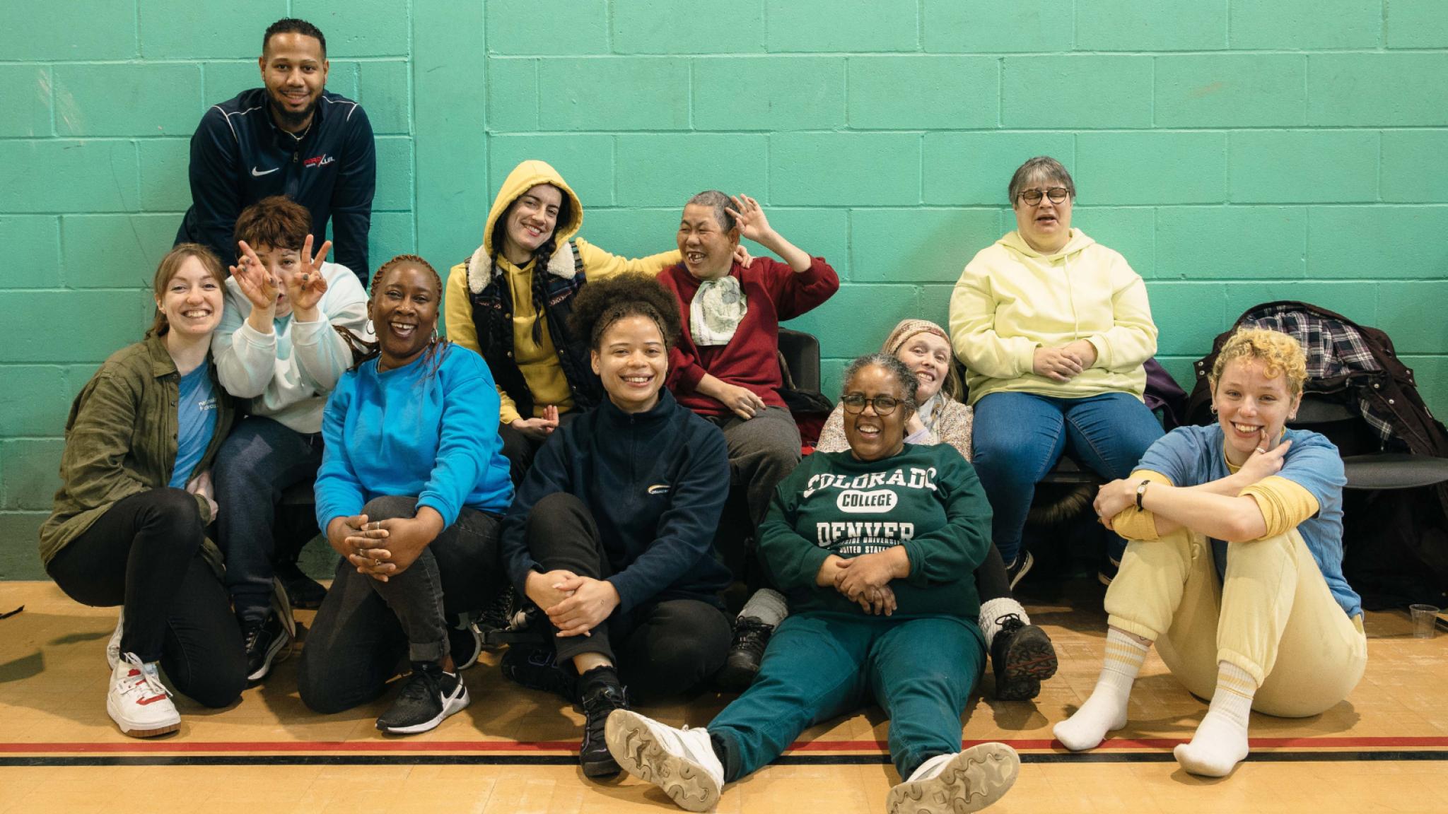 Eleven participants, staff and volunteers from Disability Sports Club pose as an informal group in a sports hall. They are all smiling and they look like they’re enjoying themselves.